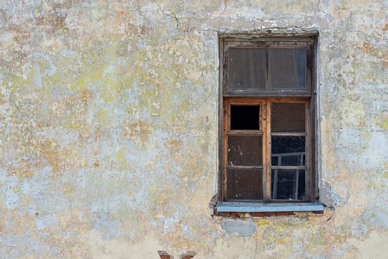 Eine alte Hauswand mit Algen und Schimmelbefall und einem kaputten Fenster